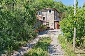 A narrow gravel path leading to a stone house with a red door, surrounded by lush greenery and potted plants. - Holiday Home 'La Casa Di Pietra - Maissana' with Mountain View, Private Terrace and Private Garden (Varese Ligure)
