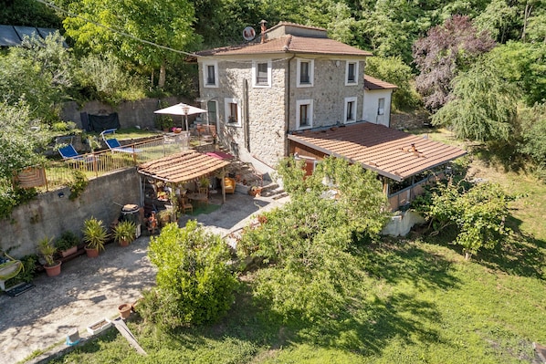 A stone house with a tiled roof, surrounded by greenery and a patio area with outdoor furniture. - Holiday Home 'La Casa Di Pietra - Maissana' with Mountain View, Private Terrace and Private Garden (Varese Ligure)