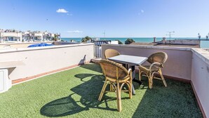 Terraza en la azotea con una mesa y sillas, vista al mar y edificios al fondo.