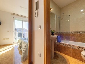 Une salle de bain avec une douche, un lavabo et des toilettes. On peut apercevoir un balcon à travers la porte.