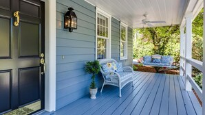 A porch with a white railing, a black door, and a blue exterior wall.