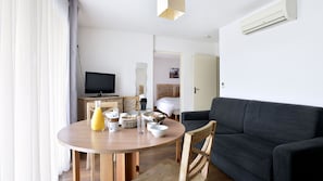 A modern living room with a round wooden table, a black sofa, and a television.