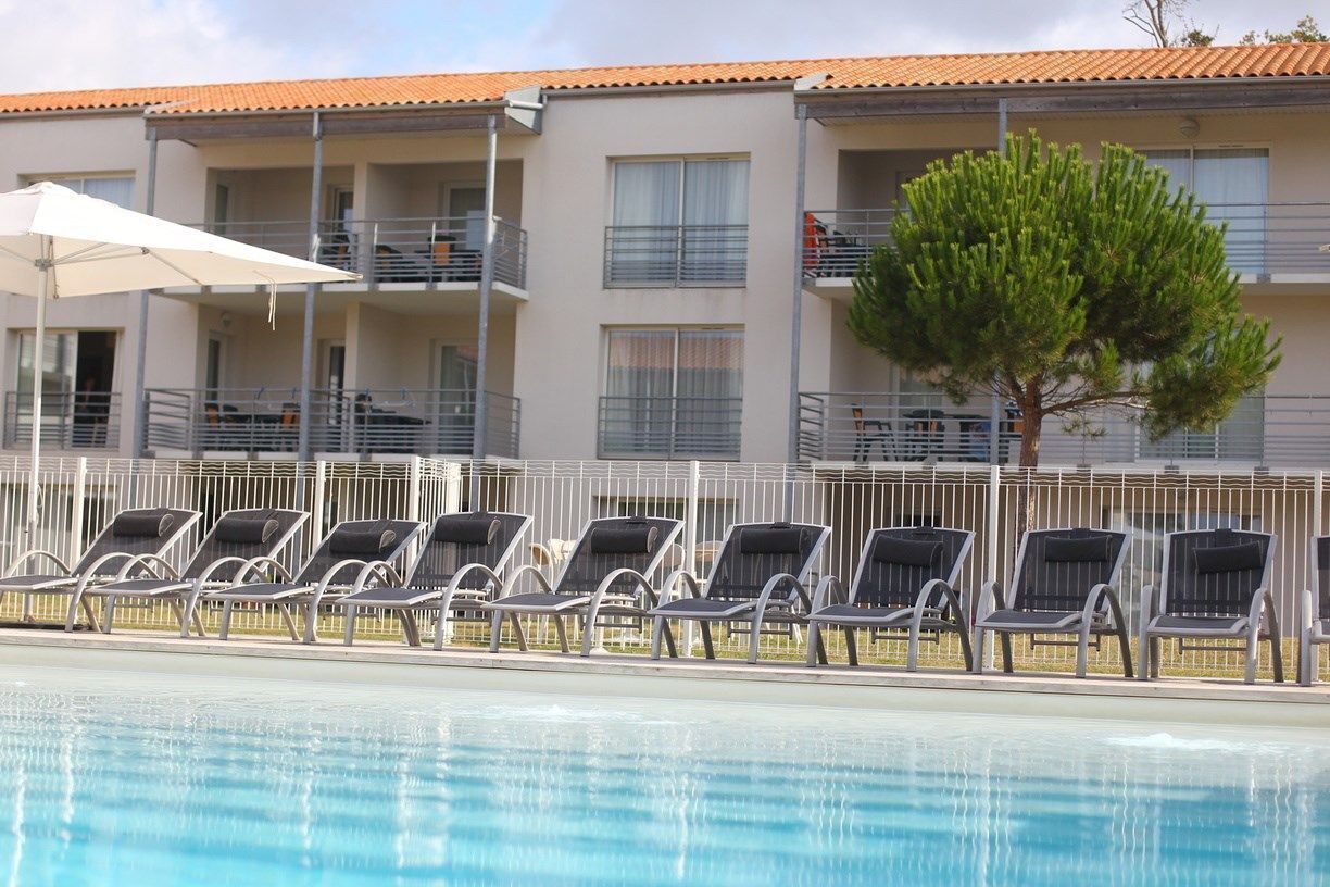 A swimming pool with lounge chairs and a building with balconies in the background.