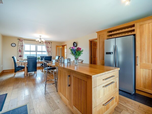A modern kitchen with wooden cabinets, a stainless steel refrigerator, and a dining area with a table and chairs.