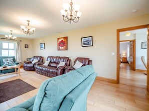 A spacious living room with leather sofas, a teal armchair, a wooden coffee table, and a chandelier.