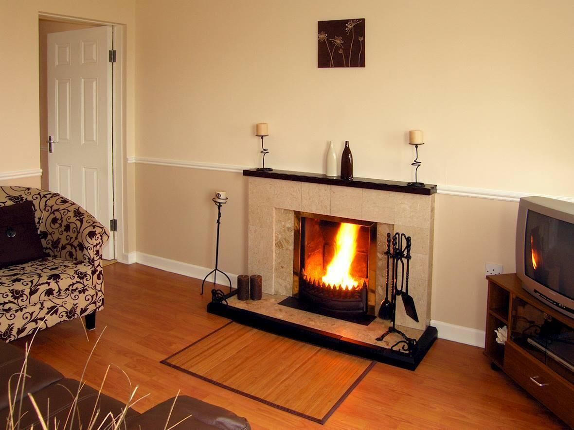 A living room with a fireplace, a sofa, a television, and a door. - 2 Bed in Castlemaine (oc-ii08066) (Aughills)