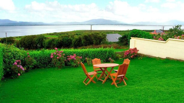 A grassy outdoor area with a table and chairs, a hedge, and a view of a body of water and distant mountains. - 2 Bed in Castlemaine (oc-ii08066) (Aughills)