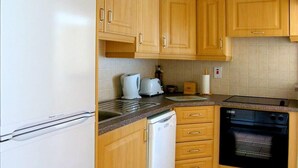A kitchen with wooden cabinets, a white refrigerator, a white dishwasher, a black oven, and a countertop with a kettle and a box labeled 'TEA'. - 2 Bed in Castlemaine (oc-ii08066) (Aughills)