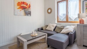 Ein modernes Wohnzimmer mit grauem Sofa, einem Holztisch und einem floralen Gemälde an der Wand.