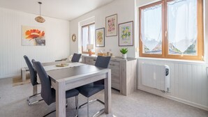 Eine moderne Küche mit Essbereich, weißen Holzwänden und großen Fenstern.