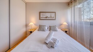 A hotel room with a bed, two bedside lamps, a framed picture of Paris, and a window with sheer curtains. - Le Halo - Avec Balcon et Parking Privé (Le Bouscat)