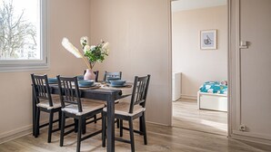 Un comedor con una mesa dispuesta para cuatro, sillas, un jarrón con flores y una ventana con vistas a árboles.