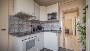 Una cocina compacta con armarios blancos, un microondas, una estufa y un salpicadero con diseño.