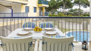 Un balcón con una mesa lista para dos personas, con vista a una piscina y un edificio con balcones.