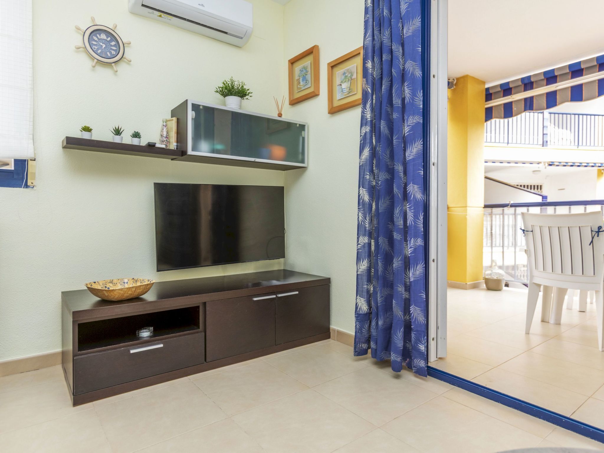 A living room with a flat-screen TV, dark wooden entertainment unit, potted plants, and a blue curtain.