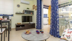 Un espacio habitable compacto con kitchenette, comedor y balcón con cortinas azules.