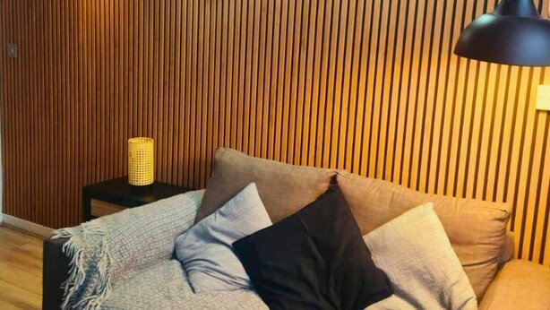 A room with a wooden slat wall, a sofa with patterned cushions, a small side table with a lamp, and a woven basket. - The Halifax Suites near Albert Dock (Liverpool)