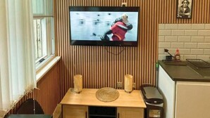 A room with a television mounted on a wall, a wooden table with a woven placemat, and a kitchen area with a sink and countertop. - The Halifax Suites near Albert Dock (Liverpool)