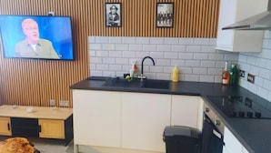 A modern kitchen with a wooden wall panel, a flat-screen TV, a sink, and a stove. - The Halifax Suites near Albert Dock (Liverpool)