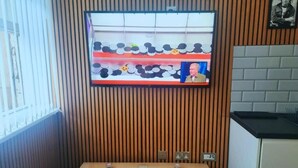 A room with a wooden slat wall, a television mounted on it, a small table with a glass, and a kitchen area with a black countertop. - The Halifax Suites near Albert Dock (Liverpool)