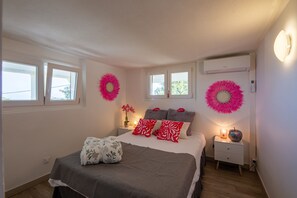 Un dormitorio con una cama, mesitas de noche, aire acondicionado instalado en la pared y dos ventanas.
