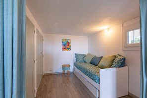 Un apartamento pequeño de una sola habitación con una cama, un taburete y un cuadro de colores en la pared, además de un ventanal.