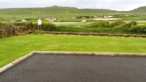 A rural landscape with a paved area in the foreground, a stone wall, and scattered houses in the background. - 3 Bed in Dingle (oc-ii00613) (Feohanagh)