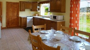 A kitchen with wooden cabinets, a stove, a microwave, and a dining table set for four with chairs. - 3 Bed in Dingle (oc-ii00613) (Feohanagh)