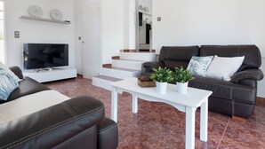 Een moderne woonkamer met een flatscreen televisie, leren banken, een salontafel met planten en een trap naar een andere kamer.