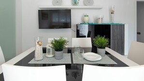 Een eethoek met een aan de muur bevestigde televisie, een flatscreen, een witte plank met decoratieve objecten, en een eettafel met stoelen.