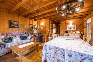 Interior de una cabaña de madera con sofá, mesa y una cama grande con colcha.