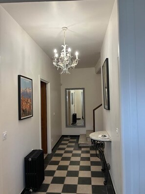 A hallway with a checkered floor, a chandelier, a mirror, a framed picture, and a radiator. - Spacious house in centre of Quillan (Quillan)
