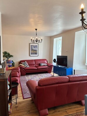 A living room with a red sofa, a patterned rug, a television, and a chandelier. - Spacious house in centre of Quillan (Quillan)