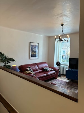 A living room with a red leather sofa, a chandelier, a framed picture on the wall, a potted plant, and a television on a stand. - Spacious house in centre of Quillan (Quillan)