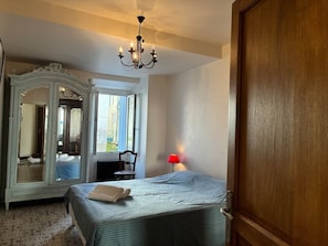A bedroom with a bed, a mirror, a chandelier, a red lamp, and a wooden door. - Spacious house in centre of Quillan (Quillan)