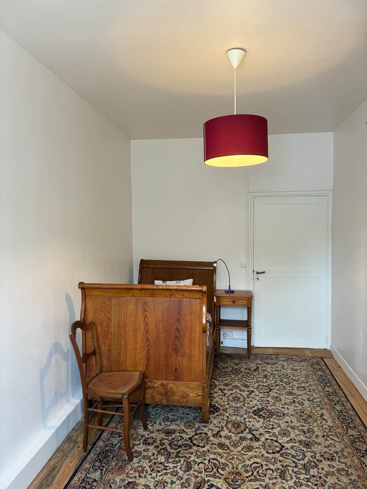 A bedroom with a wooden bed, a chair, a bedside table, and a patterned rug.