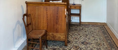A bedroom with a wooden bed, a chair, a bedside table, and a patterned rug.