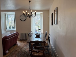 A dining room with a wooden table, chairs, a chandelier, a clock, and a radiator. - Spacious house in centre of Quillan (Quillan)