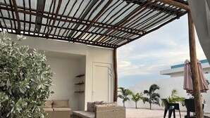 Una terrazza esterna con mobili in vimini, un pergolato e vista sul cielo.