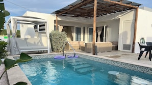 Una piscina con bordo piastrellato, circondata da sedie a sdraio e un'area patio coperta.