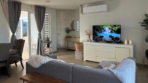 Un soggiorno moderno con un divano grigio, un tavolino in legno, un televisore su un mobile bianco e una porta scorrevole in vetro che dà su uno spazio all'aperto.