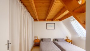 Camera da letto con due letti, travi in legno a soffitto, un quadro appeso al muro e una finestra con tende.