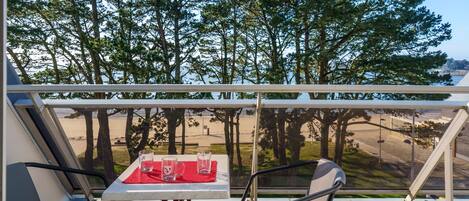 Ein Balkon mit Tisch und Stühlen, mit Blick auf einen Strand und Bäume.
