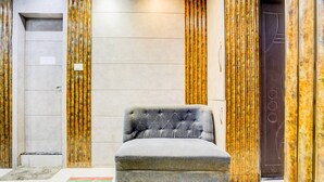 Un fauteuil capitonné gris se trouve dans un couloir aux murs de marbre et aux panneaux verticaux dorés.