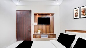 Une chambre d’hôtel avec un lit, un meuble en bois pour la télévision, un téléviseur à écran plat, une porte et deux œuvres d’art encadrées accrochées au mur.