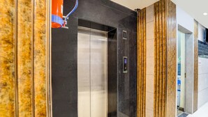 Un ascenseur à l’intérieur métallique, situé à côté d’un mur à motifs et doté d’une porte au design vertical.