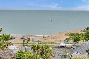A coastal view with a beach, parked cars, a boat, and a fence.
