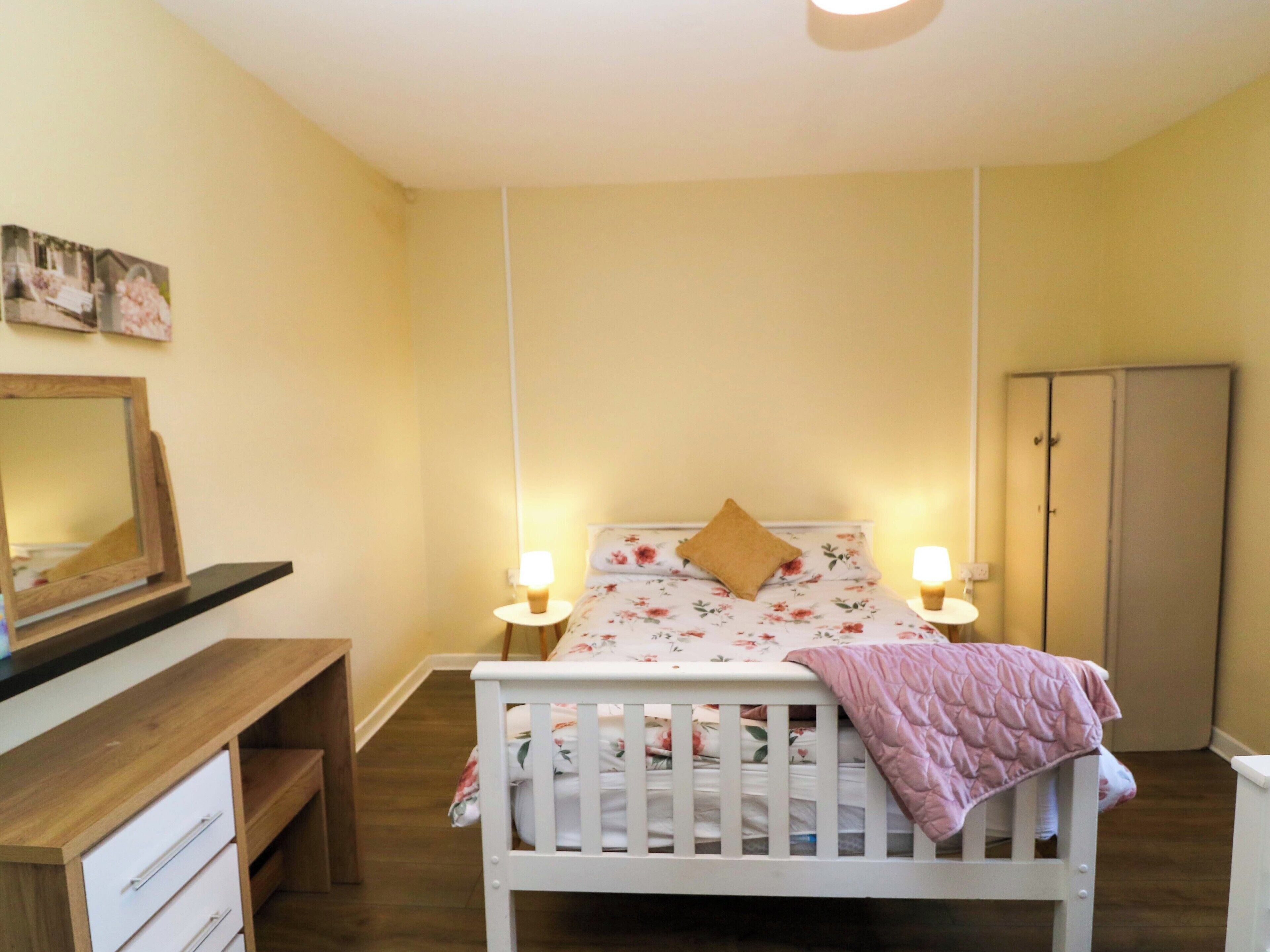 Un dormitorio con cama, lámparas de noche, cómoda de madera, espejo y armario.