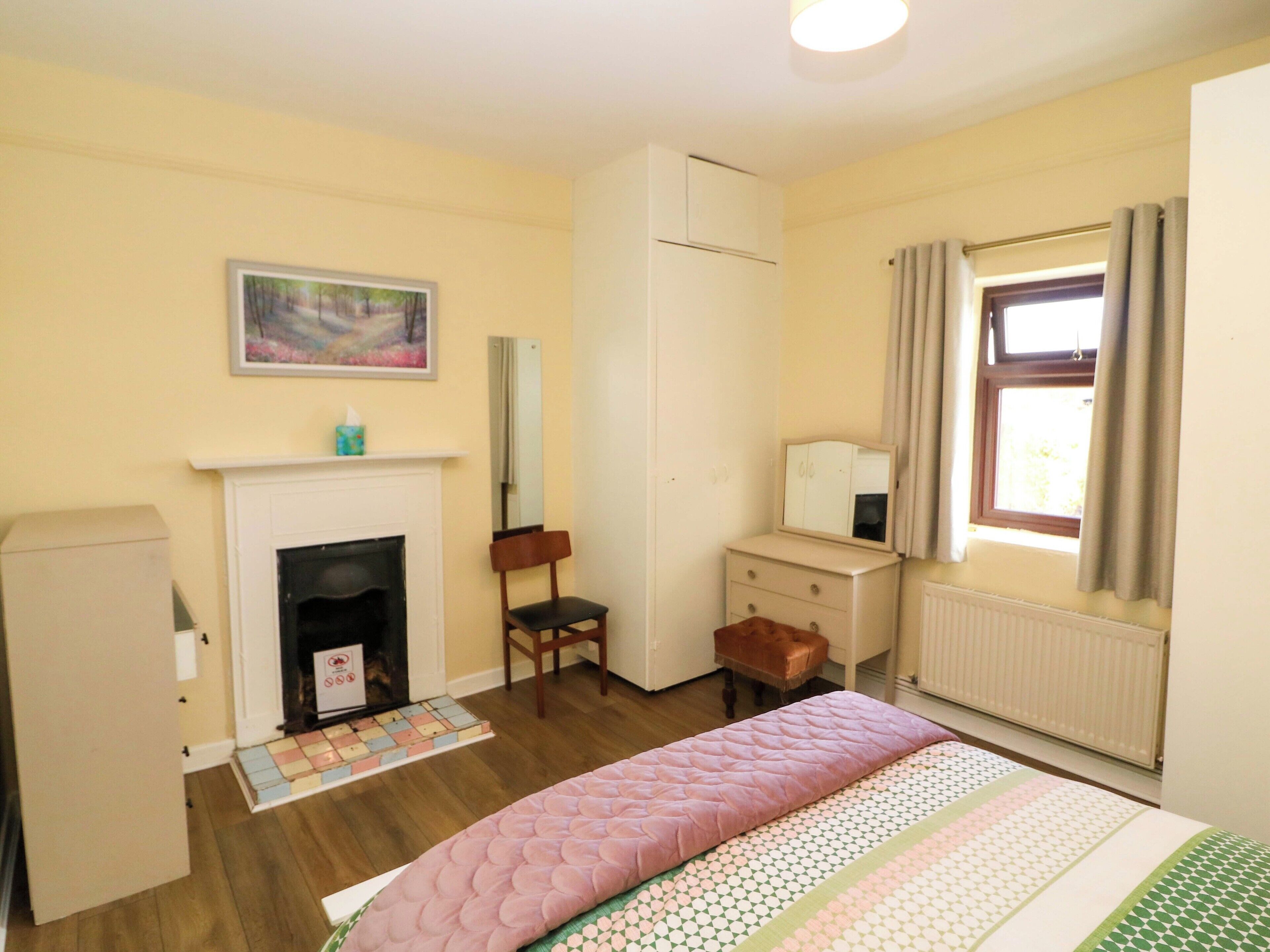 A bedroom with a bed, a fireplace, a mirror, a window with curtains, and a radiator.