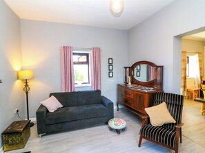 A living room with a sofa, a chair, a dresser, a lamp, and a window with curtains. - Thadg and Hannahs (Dromin)